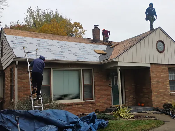 Crew tearing off shingles on a brick ranch with tarps over the landscaping