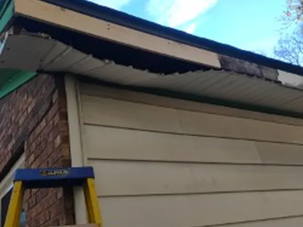 Damaged roof edge and fascia on a brick ranch with a ladder against it