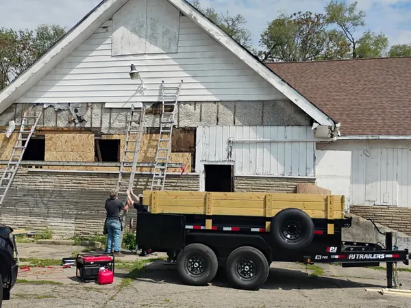 Gable-front house mid-renovation with ladders and a work trailer