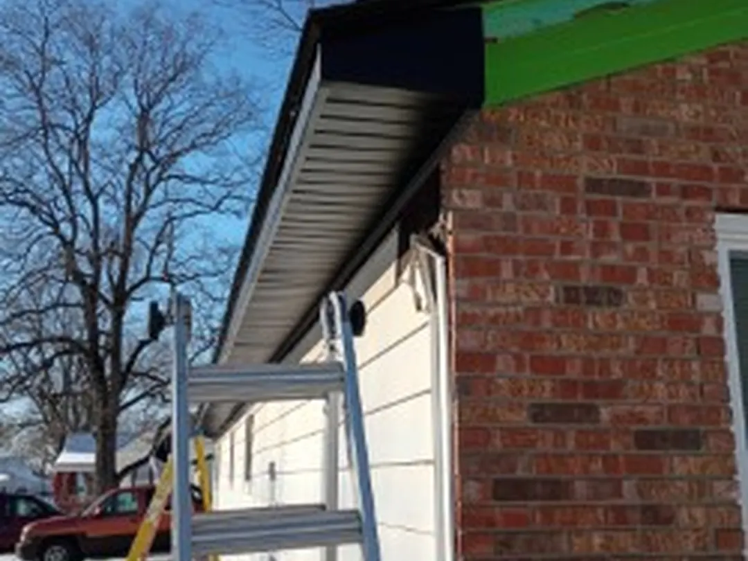 New fascia and soffit going up on the eave of a brick house with a ladder against the wall