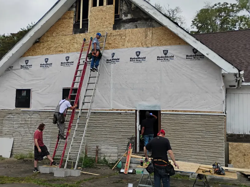 Crew on ladders wrapping a tall gable wall in house wrap before new siding