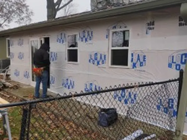 Ranch home wrapped in house wrap with a worker at the door