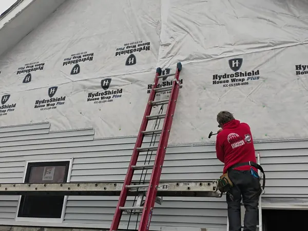Crew member on a ladder over house wrap on a gable wall