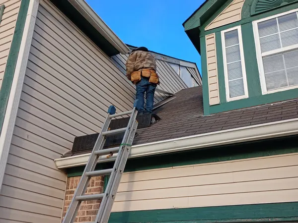 Roofer on a ladder at a dormer above a garage with green trim