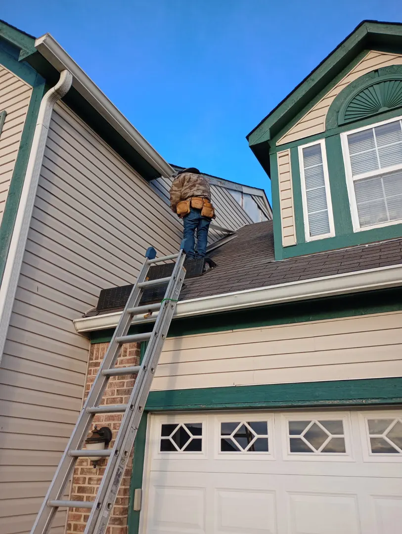 Roofer on a ladder working where a dormer with green trim meets the main roof