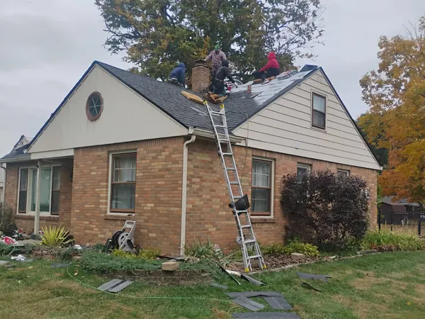 Roofer on a ladder at a brick story-and-a-half home