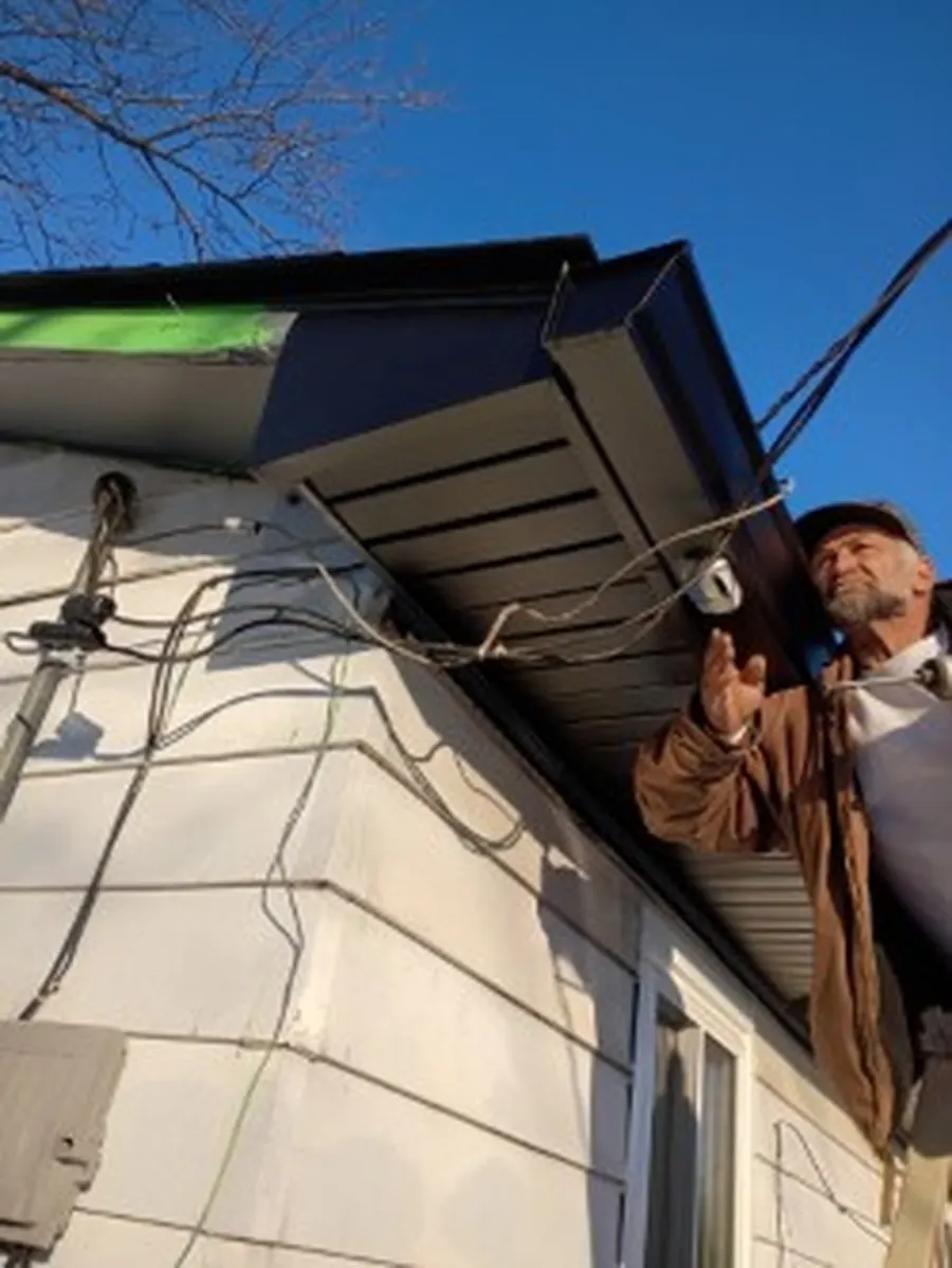 Installer fastening new soffit and a gutter run along the eave of a white house