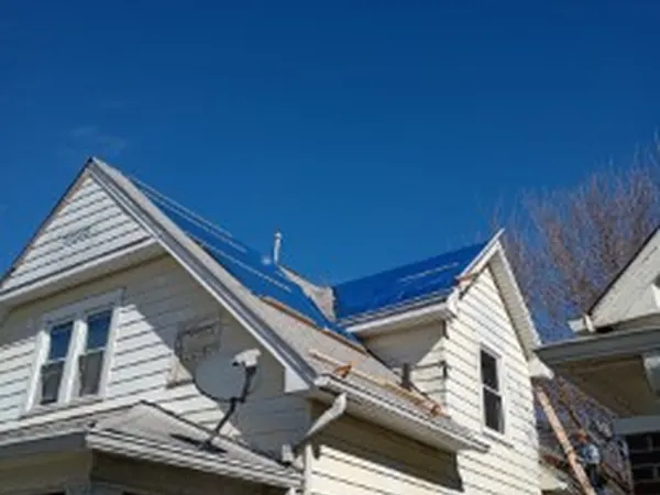 Two-story home with a blue tarp over part of the roof