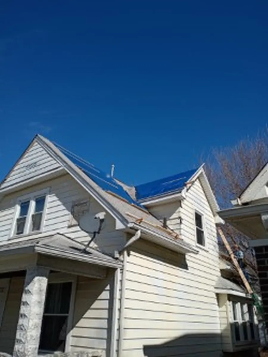 Two-story house with a blue tarp secured over part of the roof