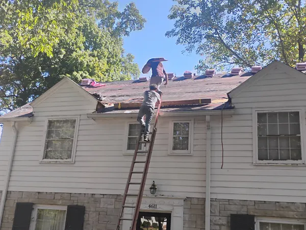 Roofer climbing a ladder to a two-story roof being stripped