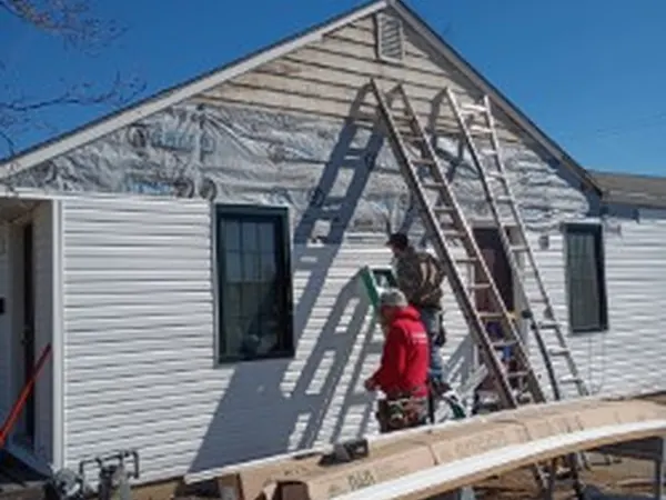 Installer on a ladder hanging white vinyl siding on a gable end