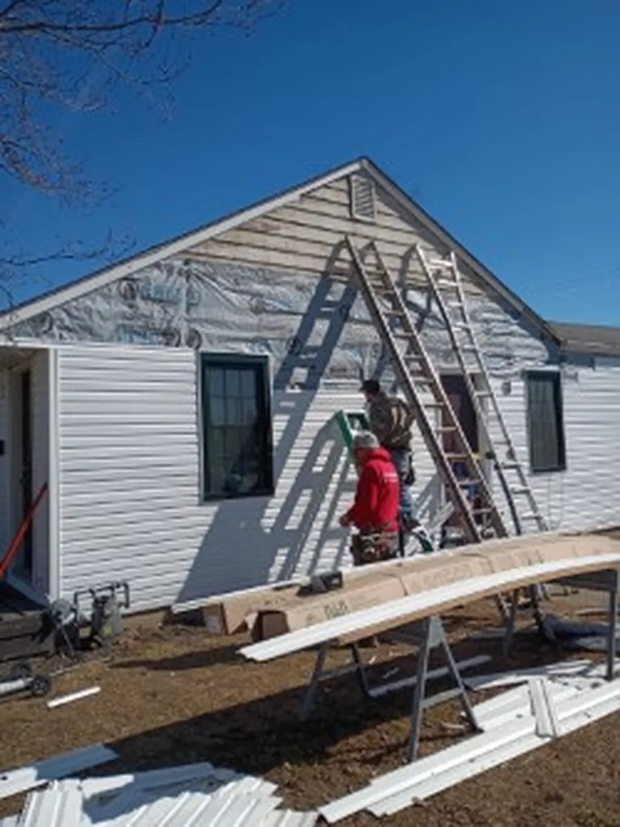 Installer on a ladder hanging new white vinyl siding on a gable end