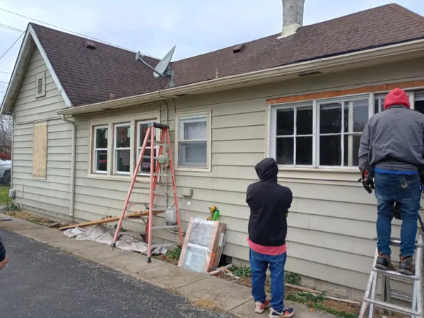 Two workers replacing windows on a tan-sided house